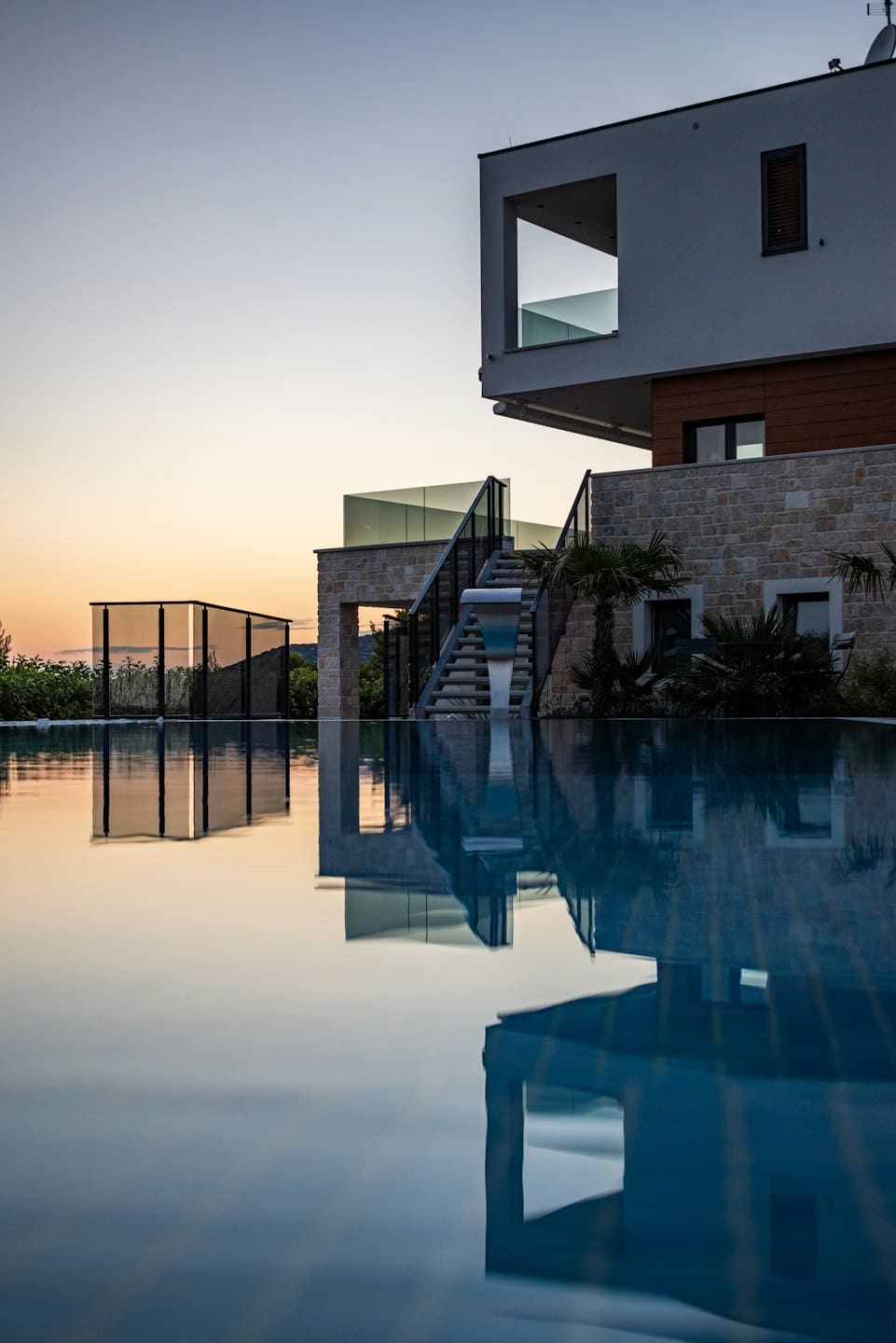 Casa di lusso con piscina a sfioro al tramonto che riflette il cielo.